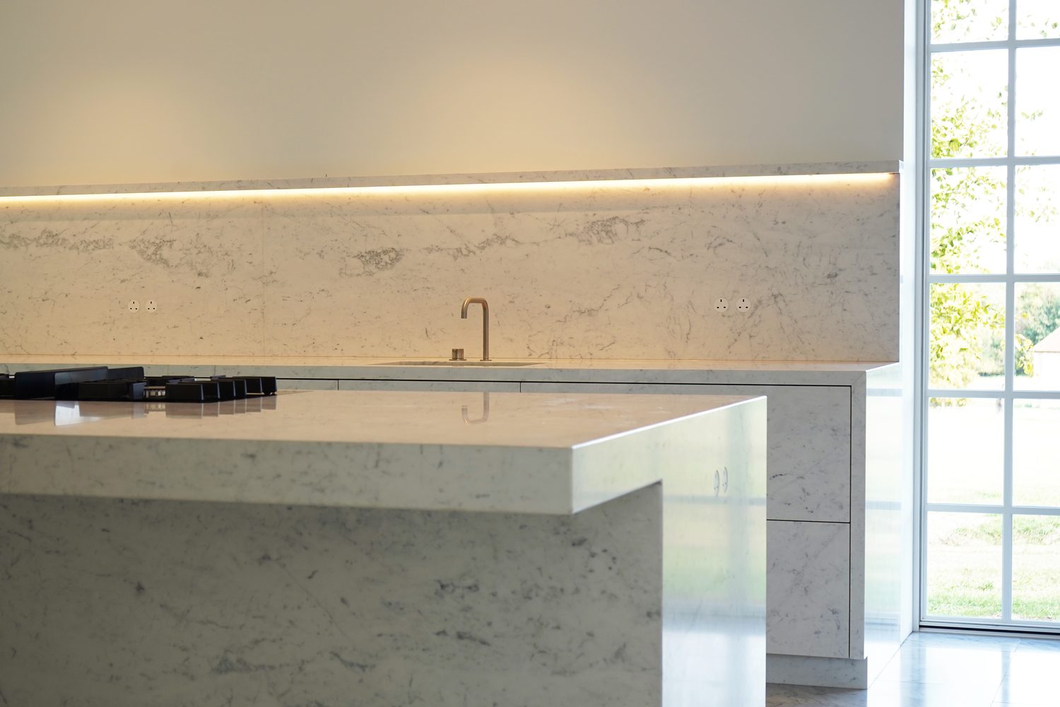 A Carrara marble island and lit splashback with an integrated sink, Oxford - Roma Marble